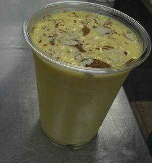 Yellow drink topped with sliced almonds in cup.