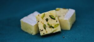 Indian sweets garnished with pistachios on teal.