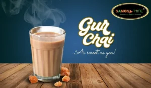 Glass of steaming chai with jaggery pieces.